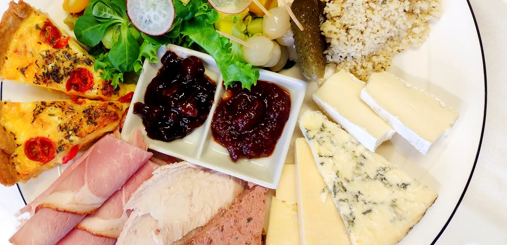 Sharing platter from Dinner Menu at Chough's Nest Hotel. Selection of cold cuts, cheeses, quiche slices, pickled onions, gherkin, salad leaves, and two types of chutney on a white plate