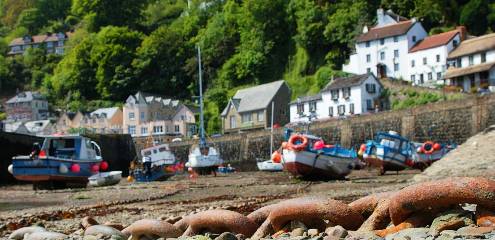 Fishing boats in Lynmouth Harbour, North Devon, resting on a rocky shore at low tide in a small coastal village.