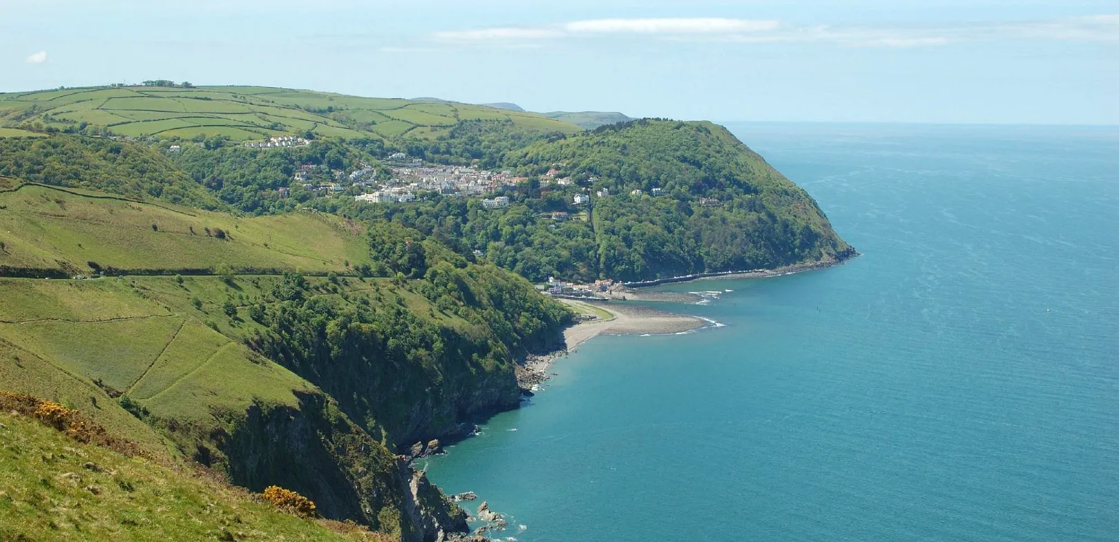 Lynton & Lynmouth, North Devon. Coastal cliffs and green hills overlooking a bay with a small village nestled among trees